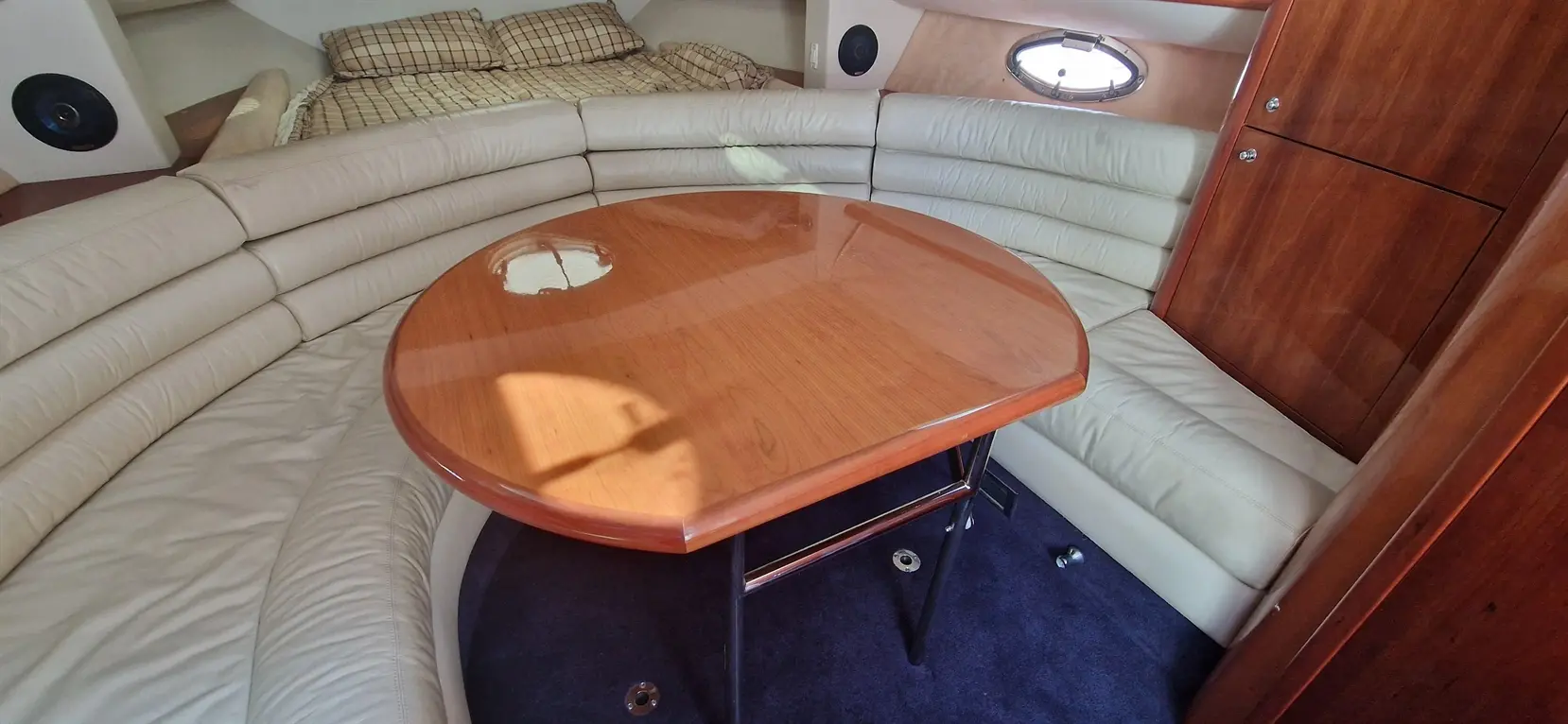 Interior of a boat featuring a circular wooden table, leather seating, and a bed in a cozy cabin setting.
